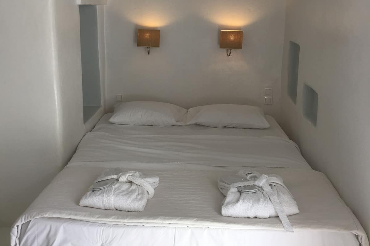 A single bed with white linens and two towels, two wall-mounted lights, and an arched doorway.