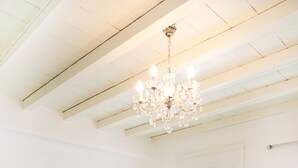 Una habitación blanca con un ventanal grande, un sofá blanco, una mesita y una araña.