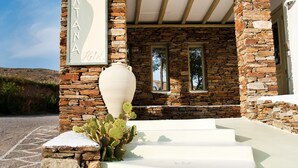 Entrada de hotel con fachada de piedra, un jarrón grande y una pérgola.