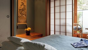A traditional Japanese-style room with tatami flooring, a low wooden bed, a shoji screen, and a view of the outdoors. - Shizuka Ryokan Japanese Country Spa & Wellness Retreat (Hepburn)