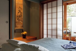 Una habitación tradicional japonesa con suelo de tatami, una cama de madera baja, un panel shoji y vistas al exterior.