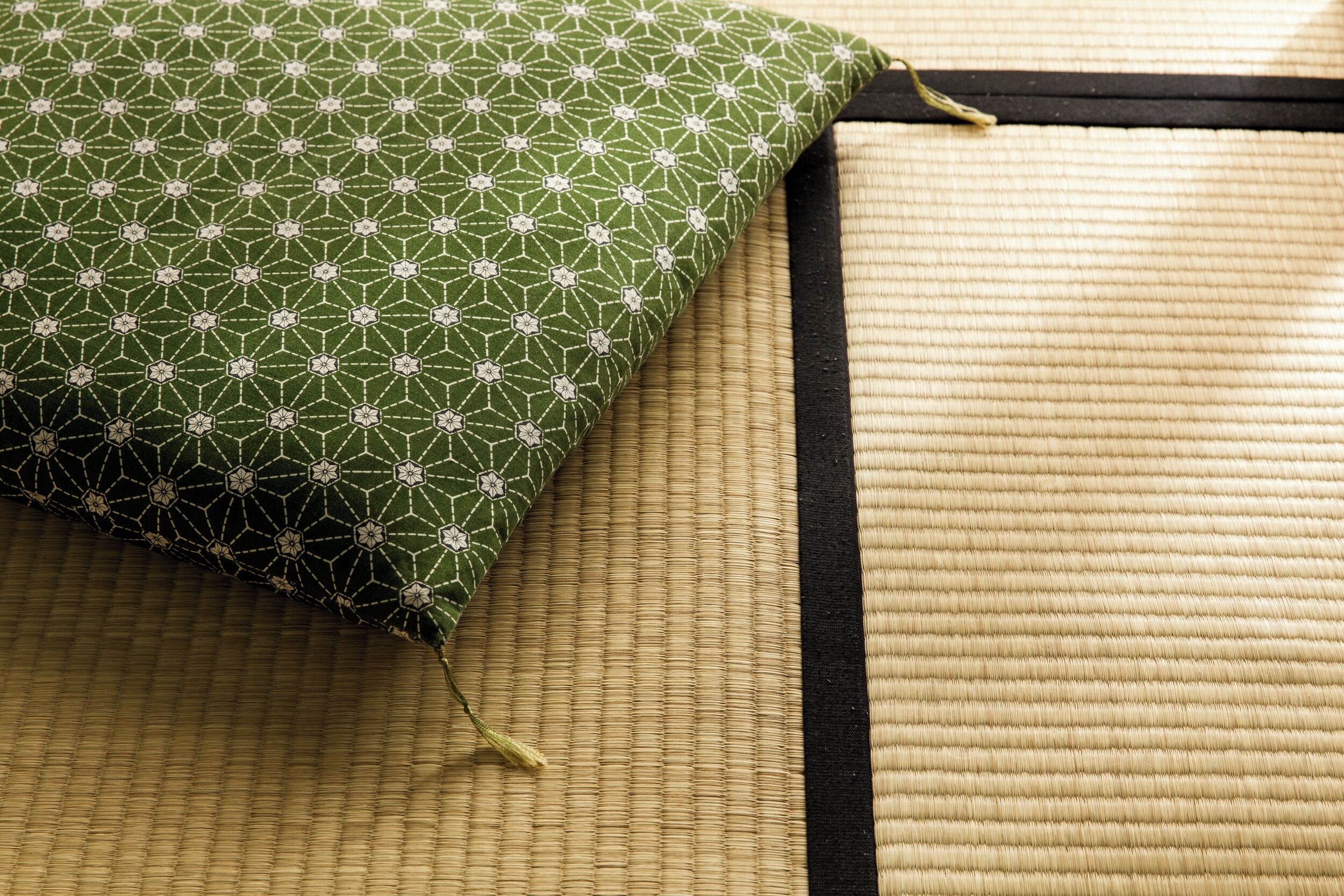 A green patterned pillow on a woven mat with a black border.