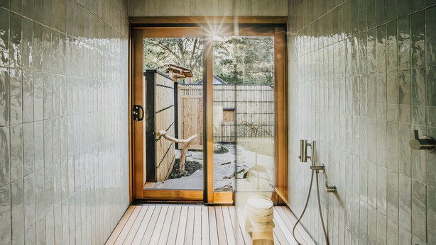 A bathroom with a wooden door leading to a garden, tiled walls, and a shower area. - Shizuka Ryokan Japanese Country Spa & Wellness Retreat (Hepburn)