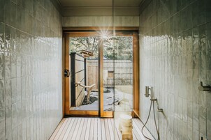 Un baño con puerta de madera que da a un jardín, paredes con azulejos y zona de ducha.
