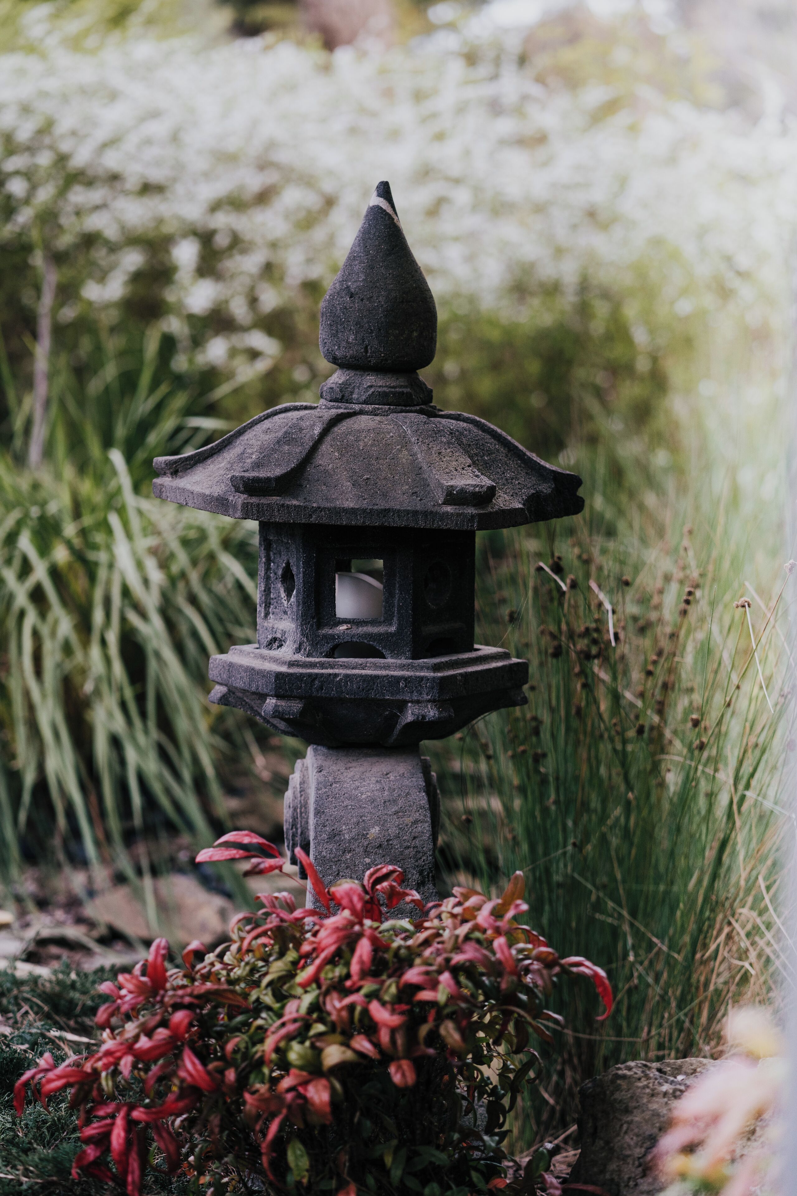 A stone lantern in a garden with tall grass and red foliage.