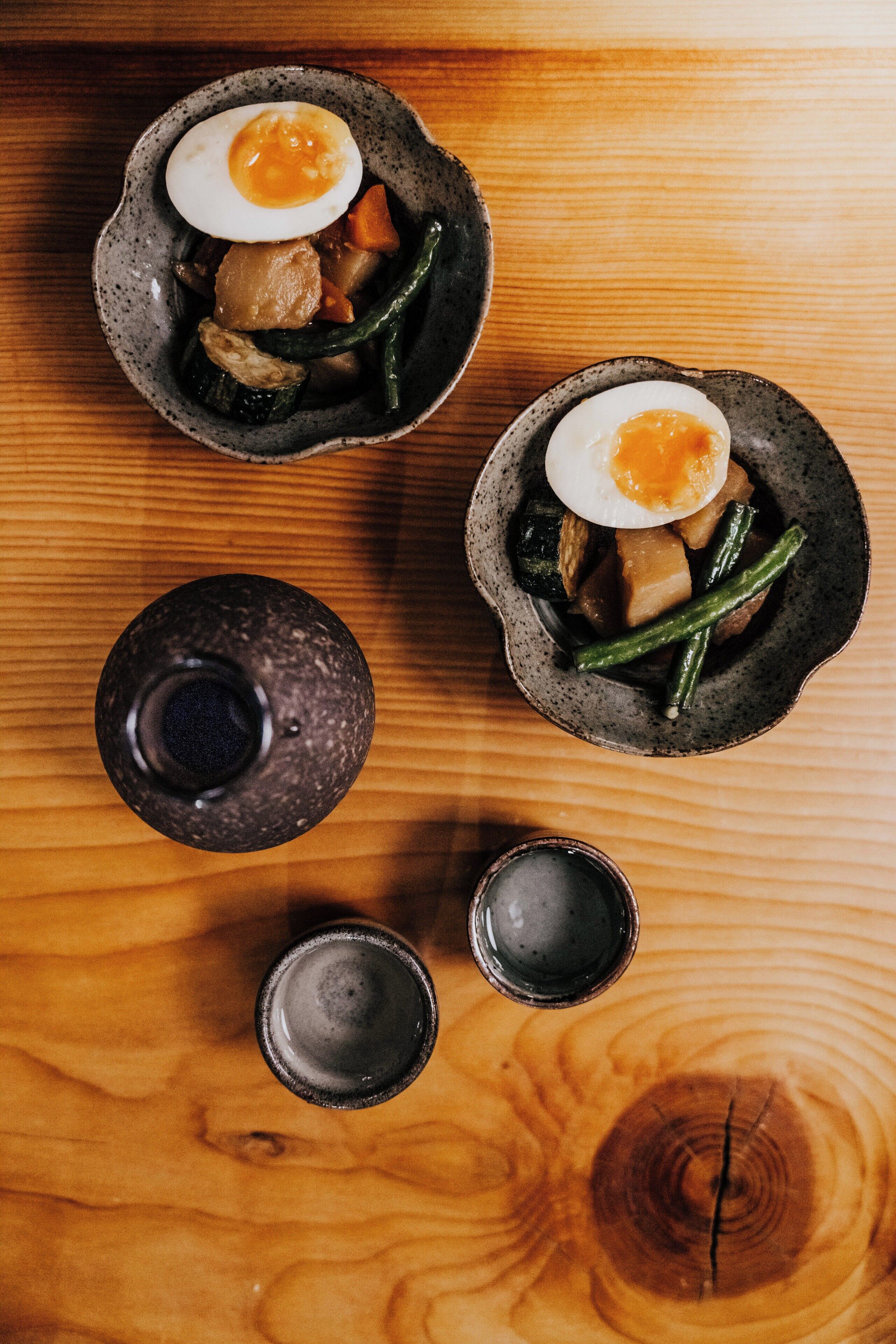 Una mesa de madera con tres cuencos de cerámica llenos de comida, un recipiente pequeño y dos tazas pequeñas.