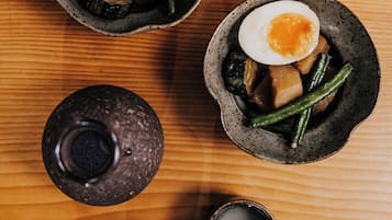 Una mesa de madera con tres cuencos de cerámica llenos de comida, un recipiente pequeño y dos tazas pequeñas.