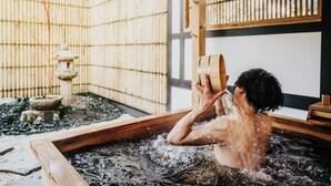 A person in a wooden hot spring bath with a bamboo fence and a stone lantern in the background. - Shizuka Ryokan Japanese Country Spa & Wellness Retreat (Hepburn)