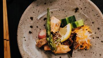 A table with a plate of food, including noodles, vegetables, and a slice of lemon.