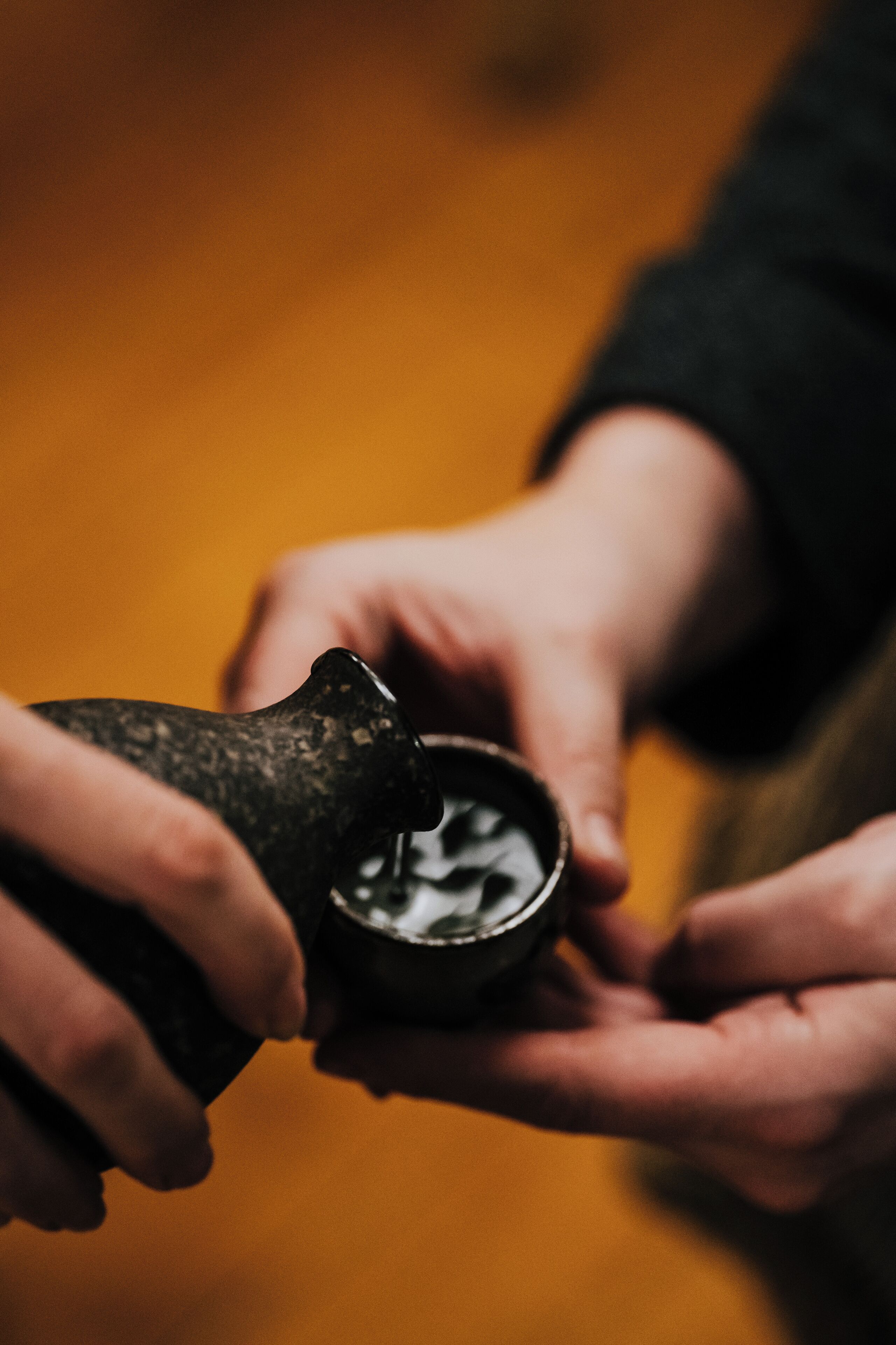 A close-up of hands holding a bottle with a dark, textured label.