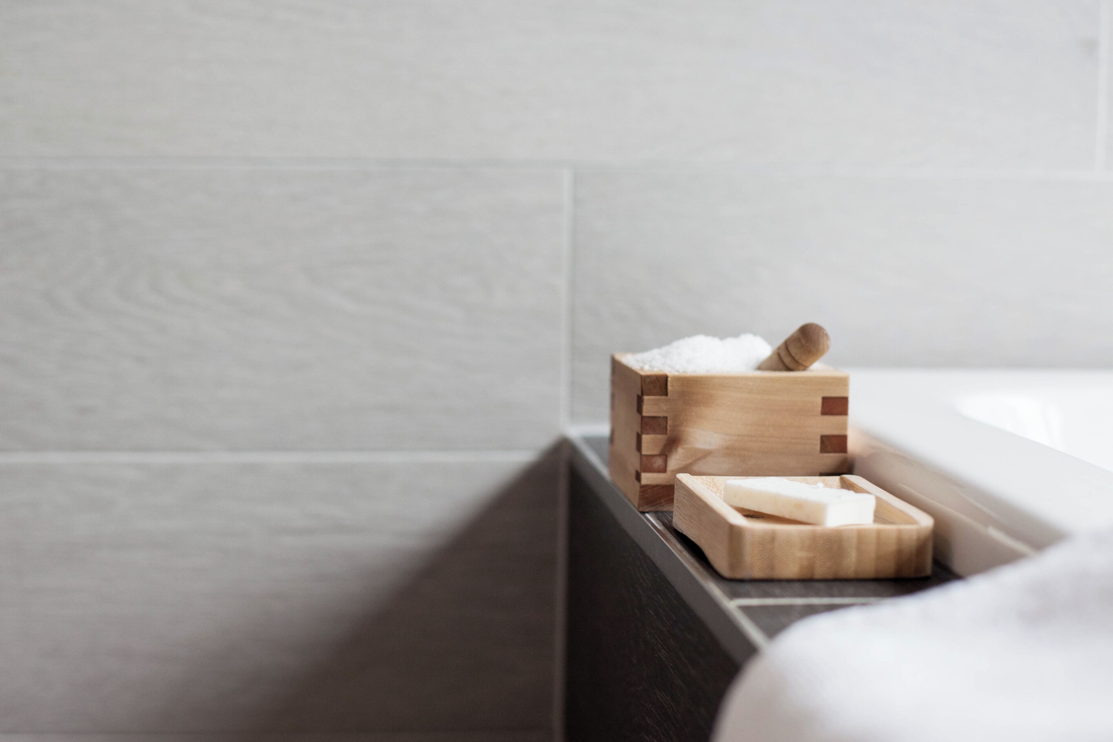 Un porte-savon en bois contenant un savon et un pain de savon, posé sur un comptoir foncé dans une salle de bain.