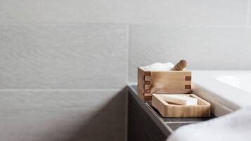 Un jabonera de madera con jabón y una barra de jabón sobre una encimera oscura en un baño.