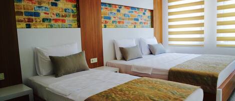 A hotel room with two beds, a colorful brick-patterned wall, and a window with horizontal blinds.