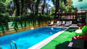 A swimming pool with a metal ladder, surrounded by green artificial turf and white lounge chairs. - Ale Boutique Hotel (Konyaalti)