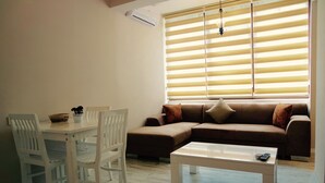 A living room with a brown sofa, white chairs, a white coffee table, and a large window with blinds. - Ale Boutique Hotel (Konyaalti)
