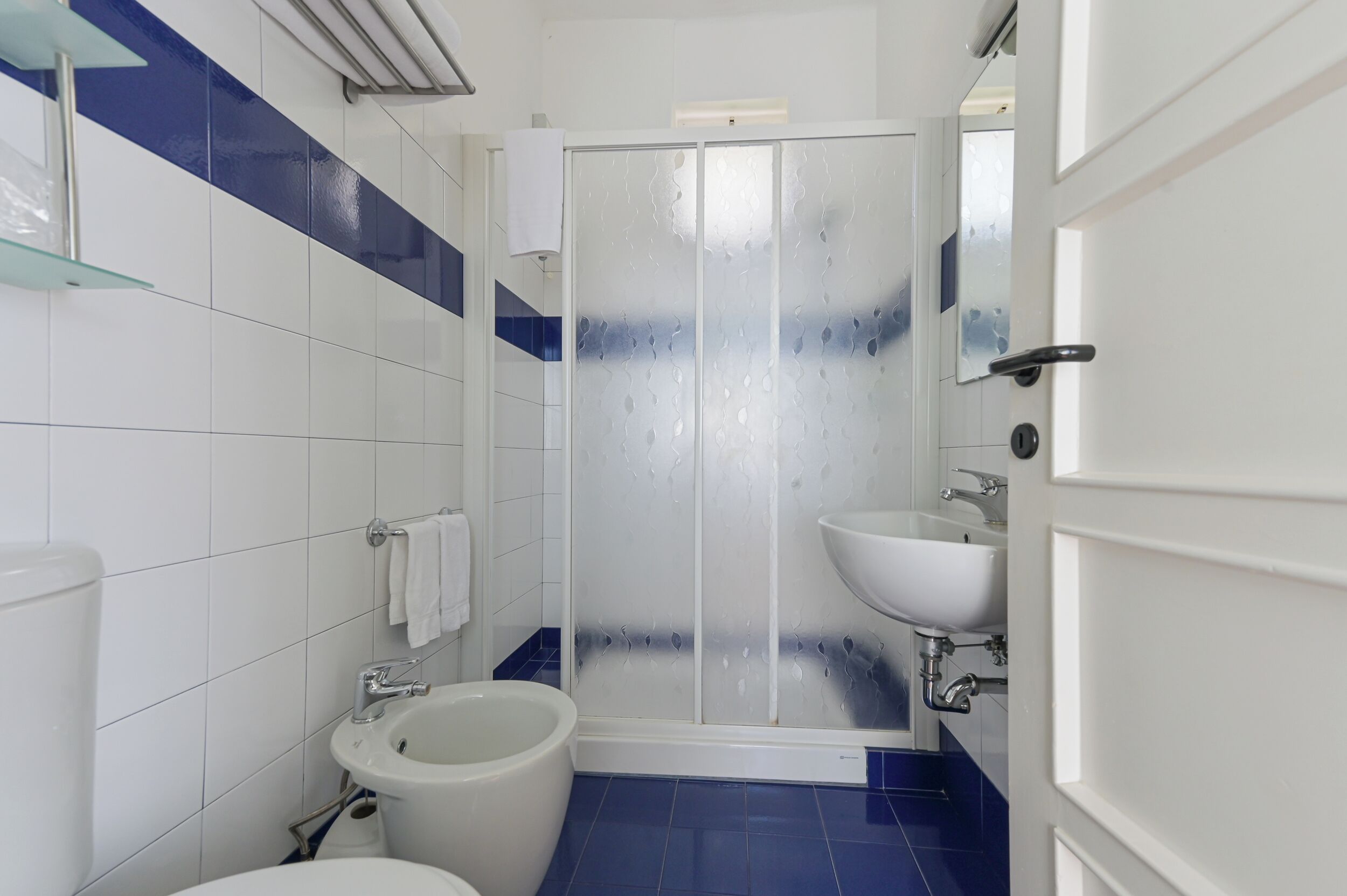 Une salle de bain comprenant des toilettes, un bidet, un lavabo et une douche à parois en verre.