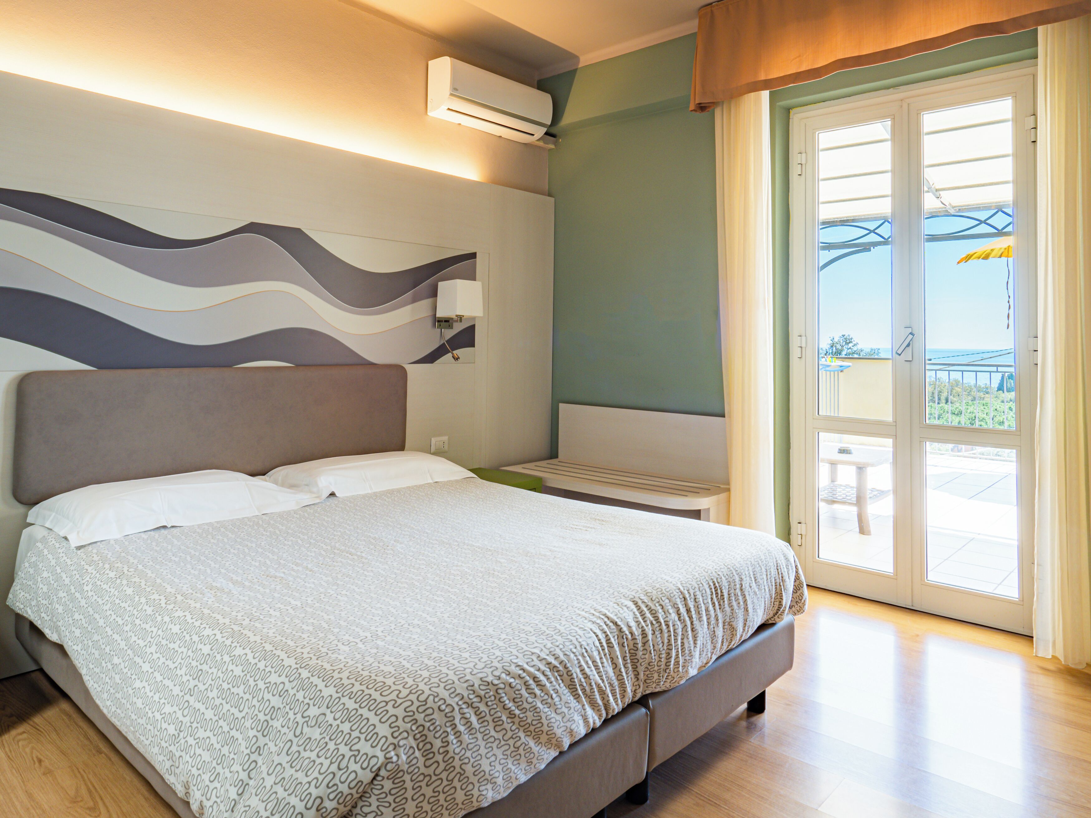 A bedroom with a bed, a bedside table, an air conditioning unit, and a view of the outdoors.