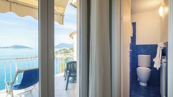 A balcony with a view of the sea and mountains, a toilet, and a chair.