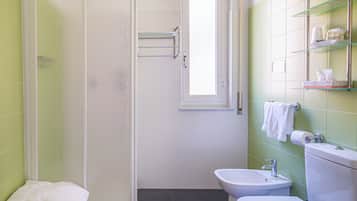 A bathroom with a shower, toilet, bidet, and shelves with toiletries.