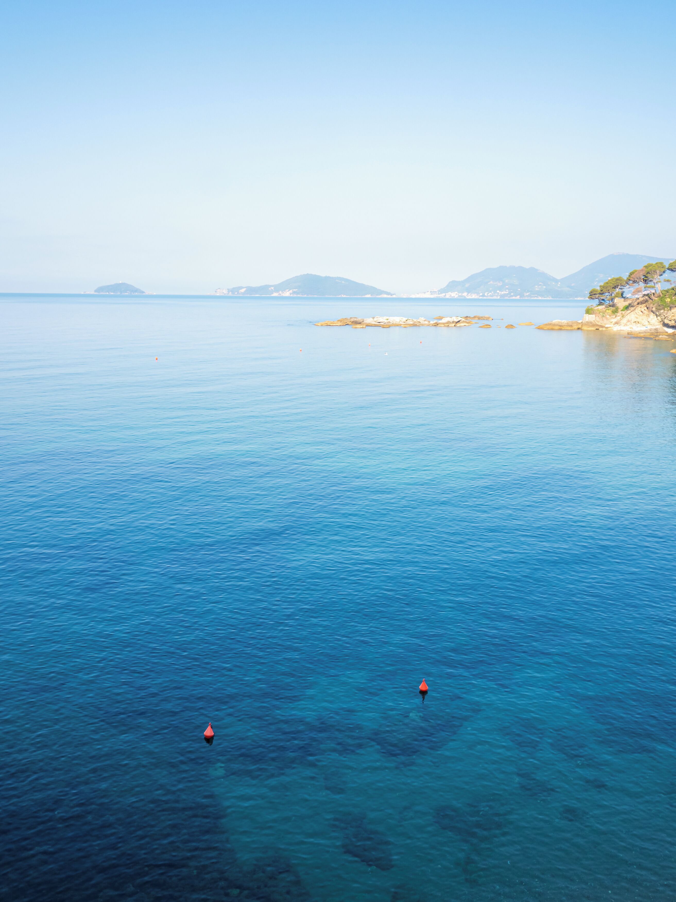 A coastal view with clear blue waters, distant landforms, and buoys.
