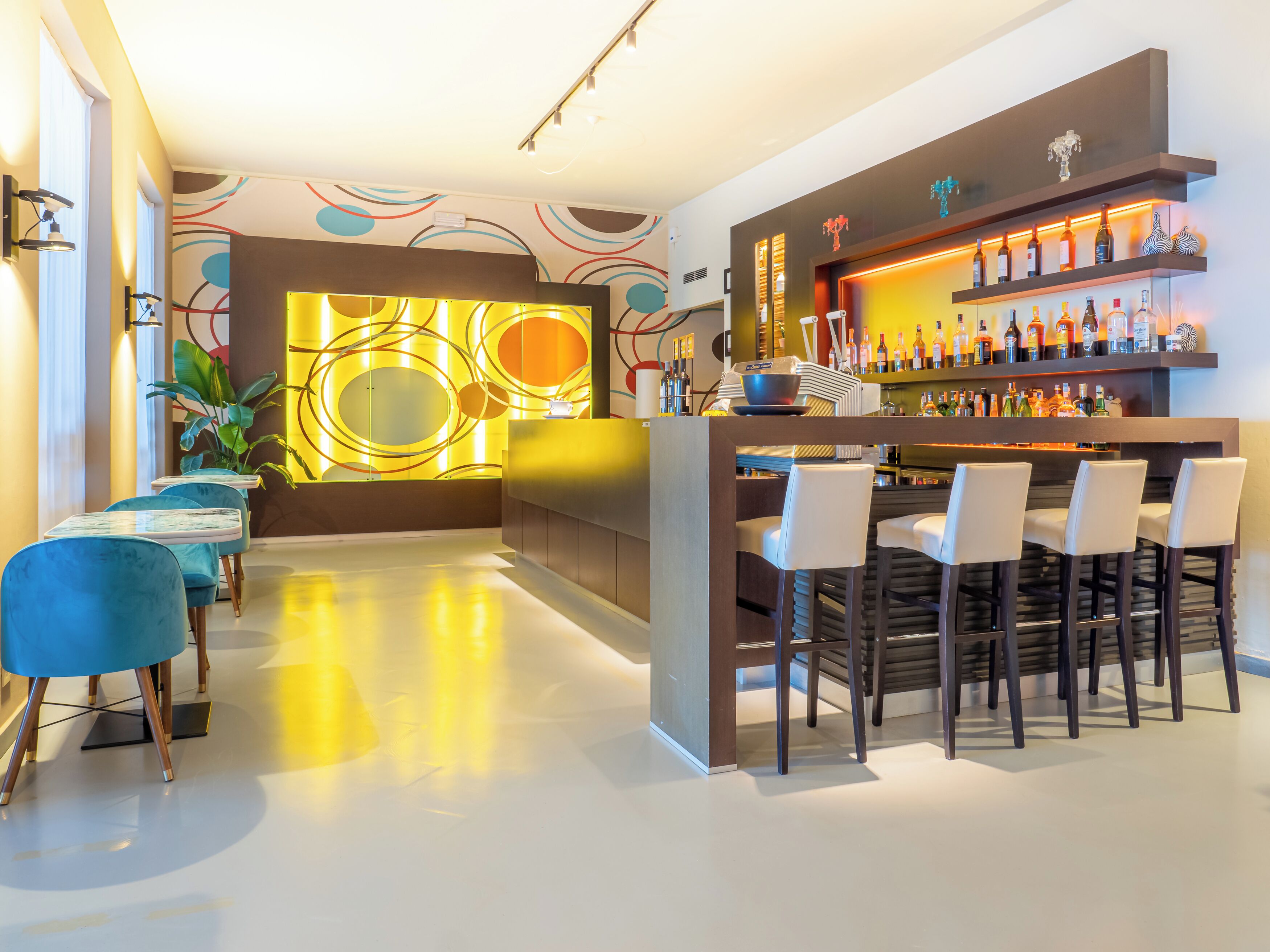 A modern bar area with a bar counter, multiple seating options, and a variety of bottles.