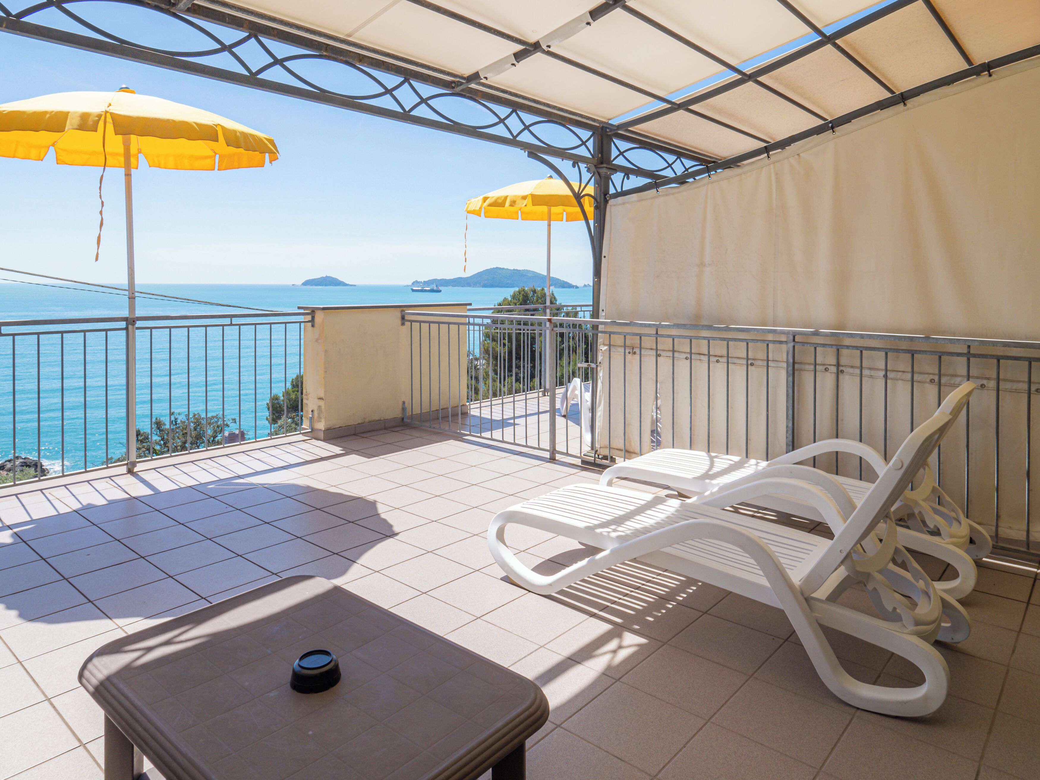 A balcony with two white lounge chairs, a small table, and two yellow umbrellas.