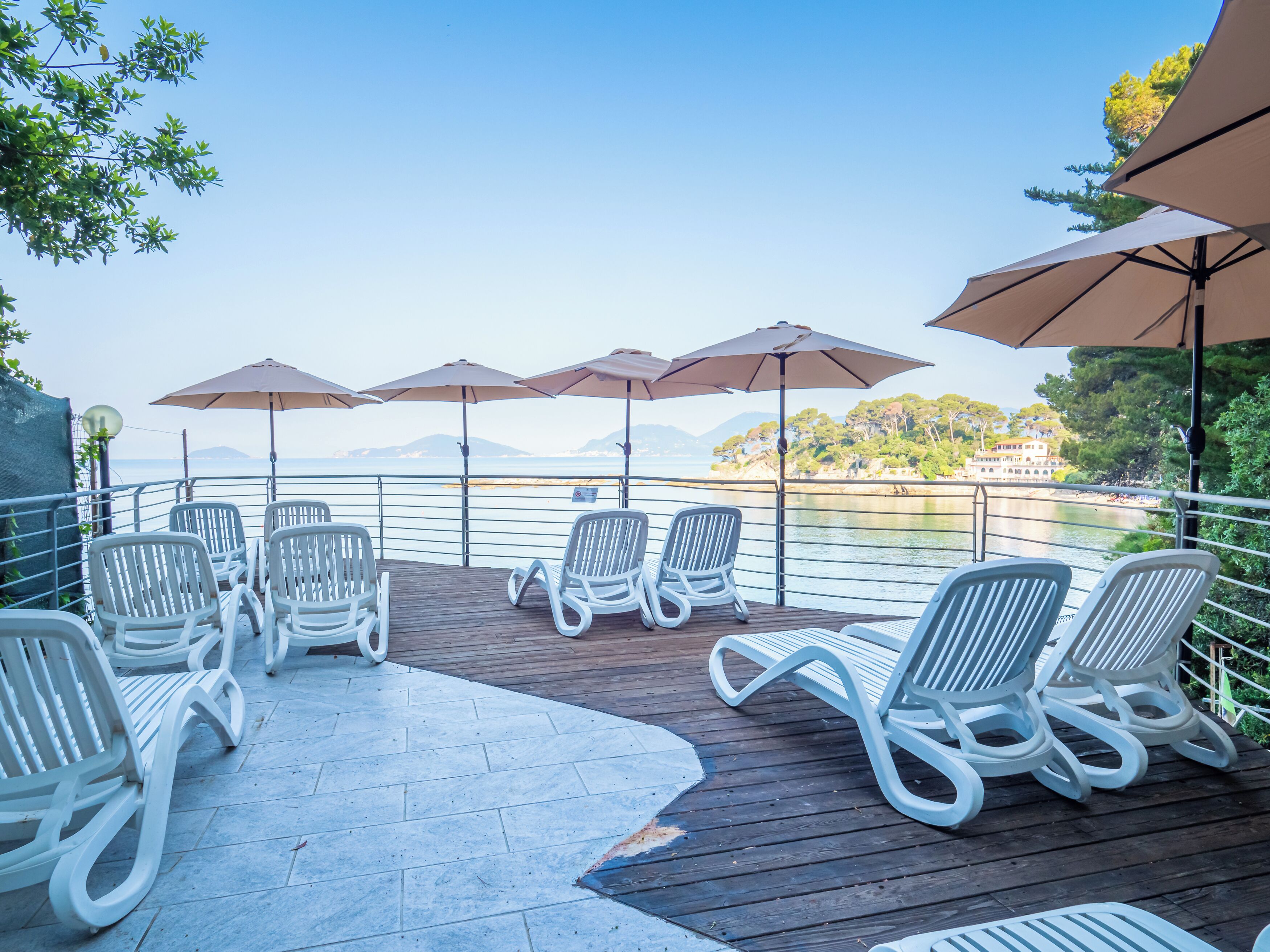 A deck with white lounge chairs and umbrellas overlooking a body of water with a distant island.