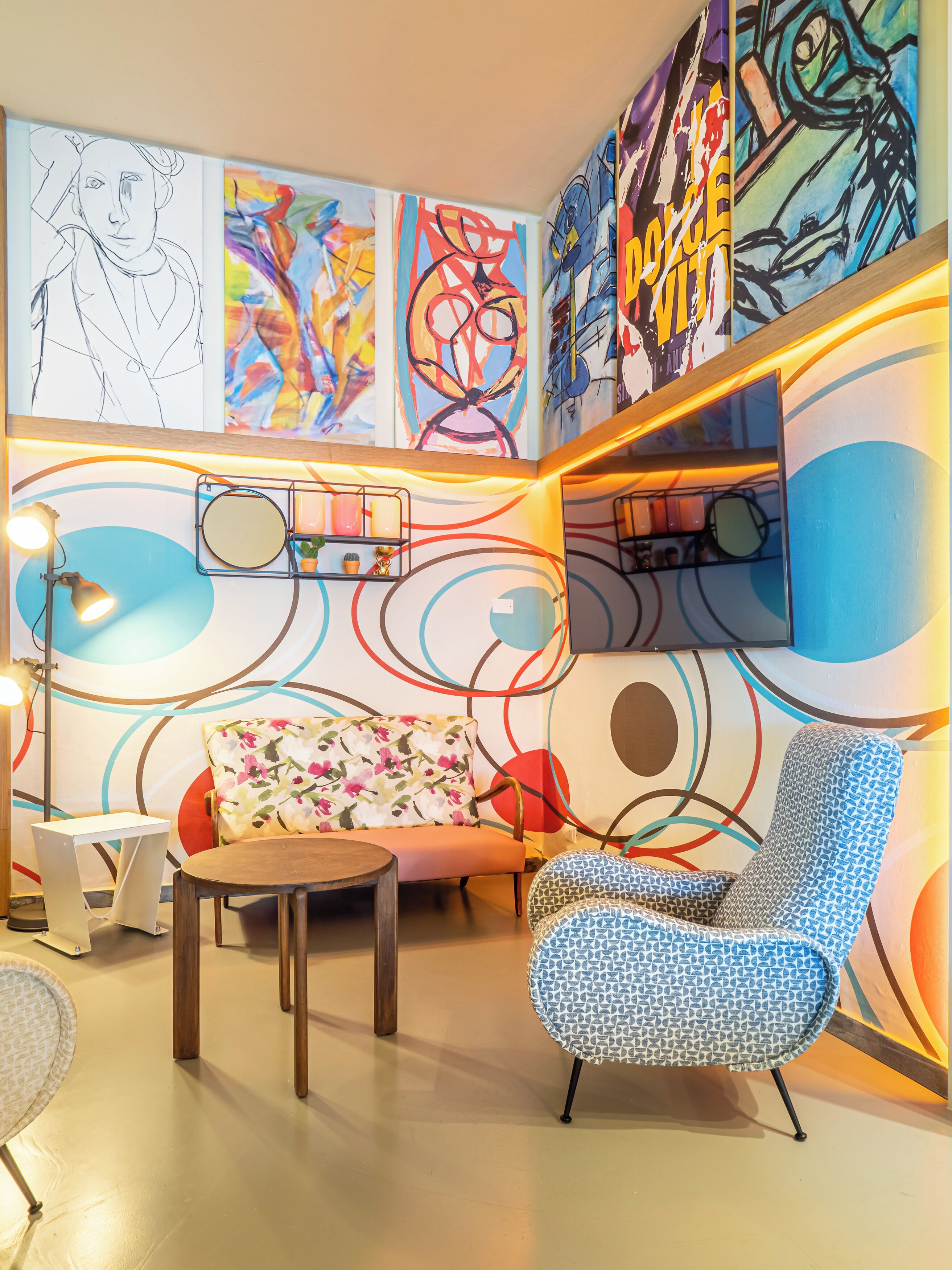 Ein modernes Wohnzimmer mit abstrakter Wandkunst, einem Sofa, einem gemusterten Sessel, einem kleinen Tisch und einer Stehlampe.