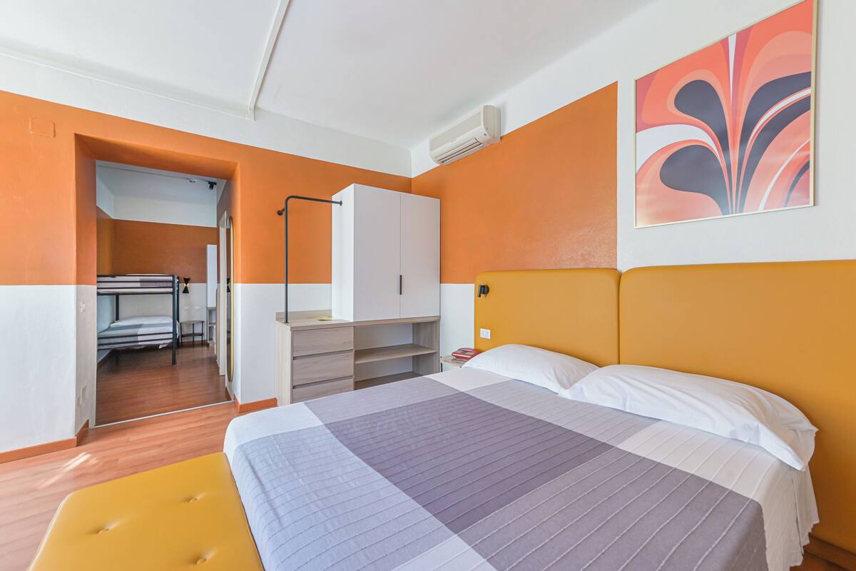 A hotel room with a bed, a wardrobe, a desk, and a view of the hallway.