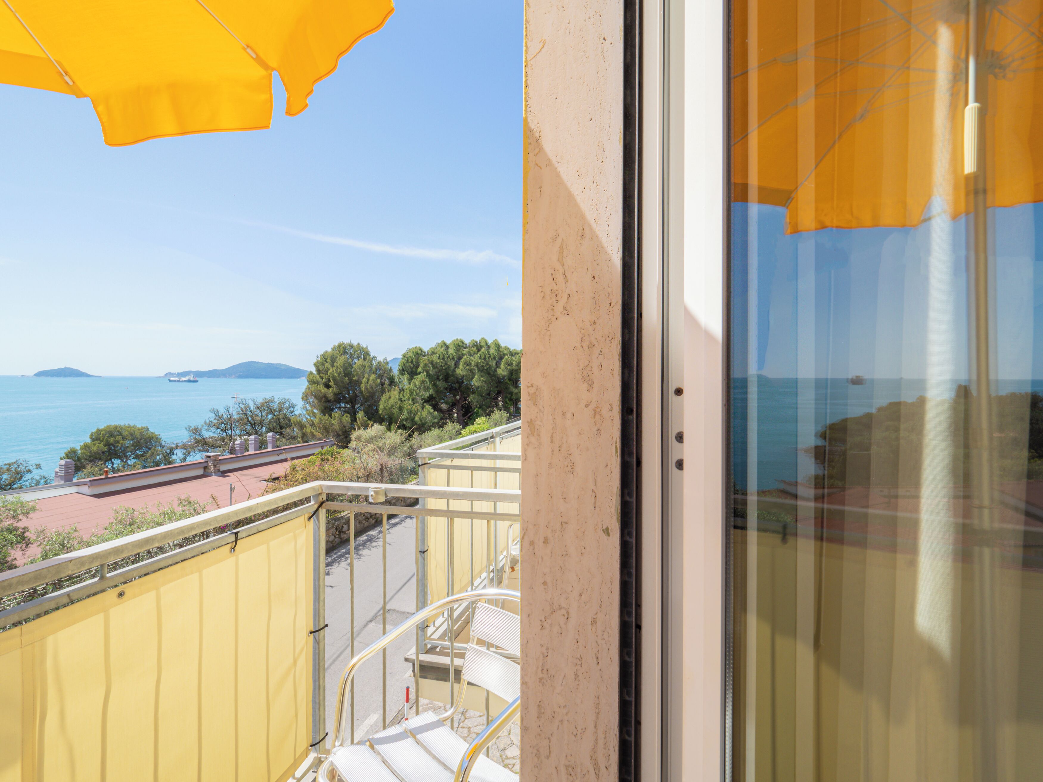 A balcony with a view of the sea, a yellow railing, and a glass door.
