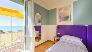 A room with a bed, a mirror, a small table, a chair, and a balcony with an umbrella.