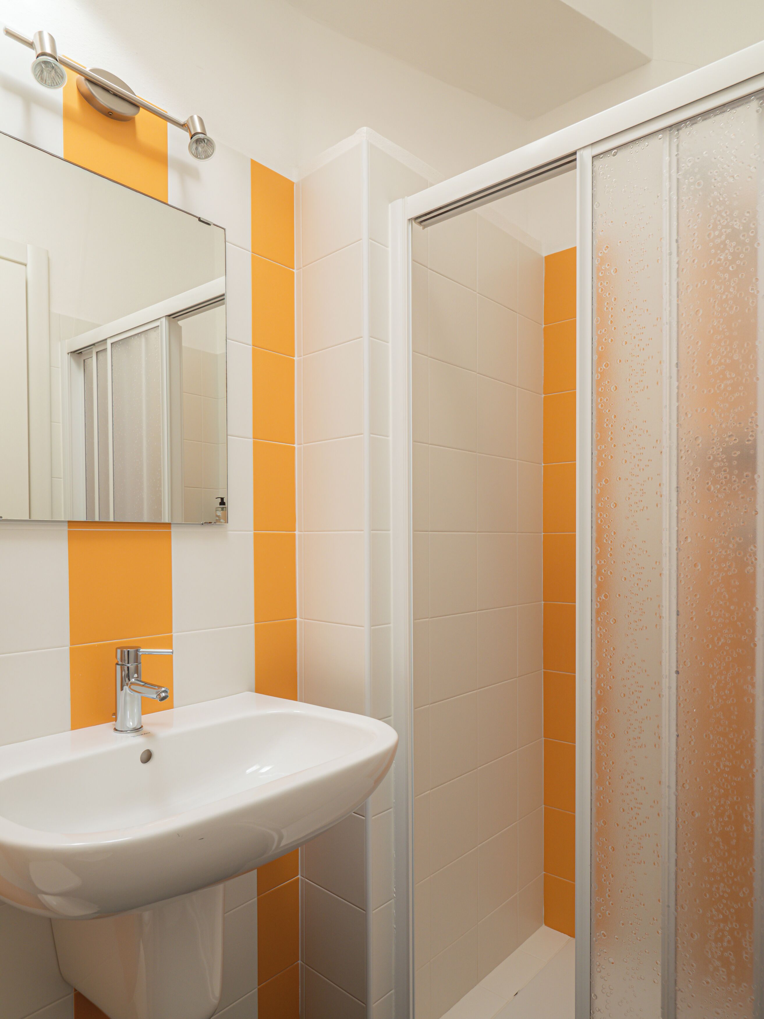 A bathroom with a white sink, a mirror, and orange tiles.