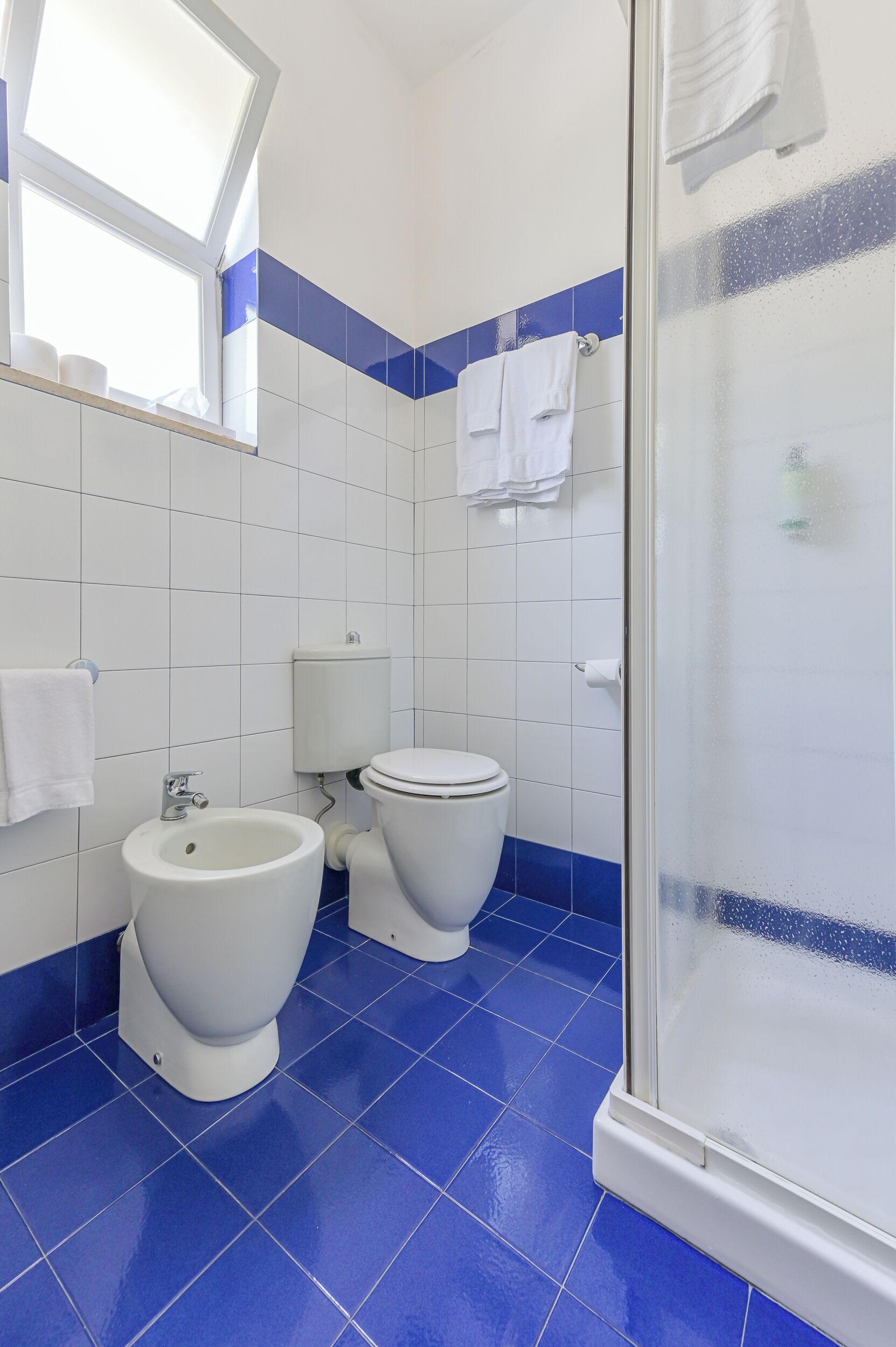 A bathroom with two toilets, a bidet, and a shower area.