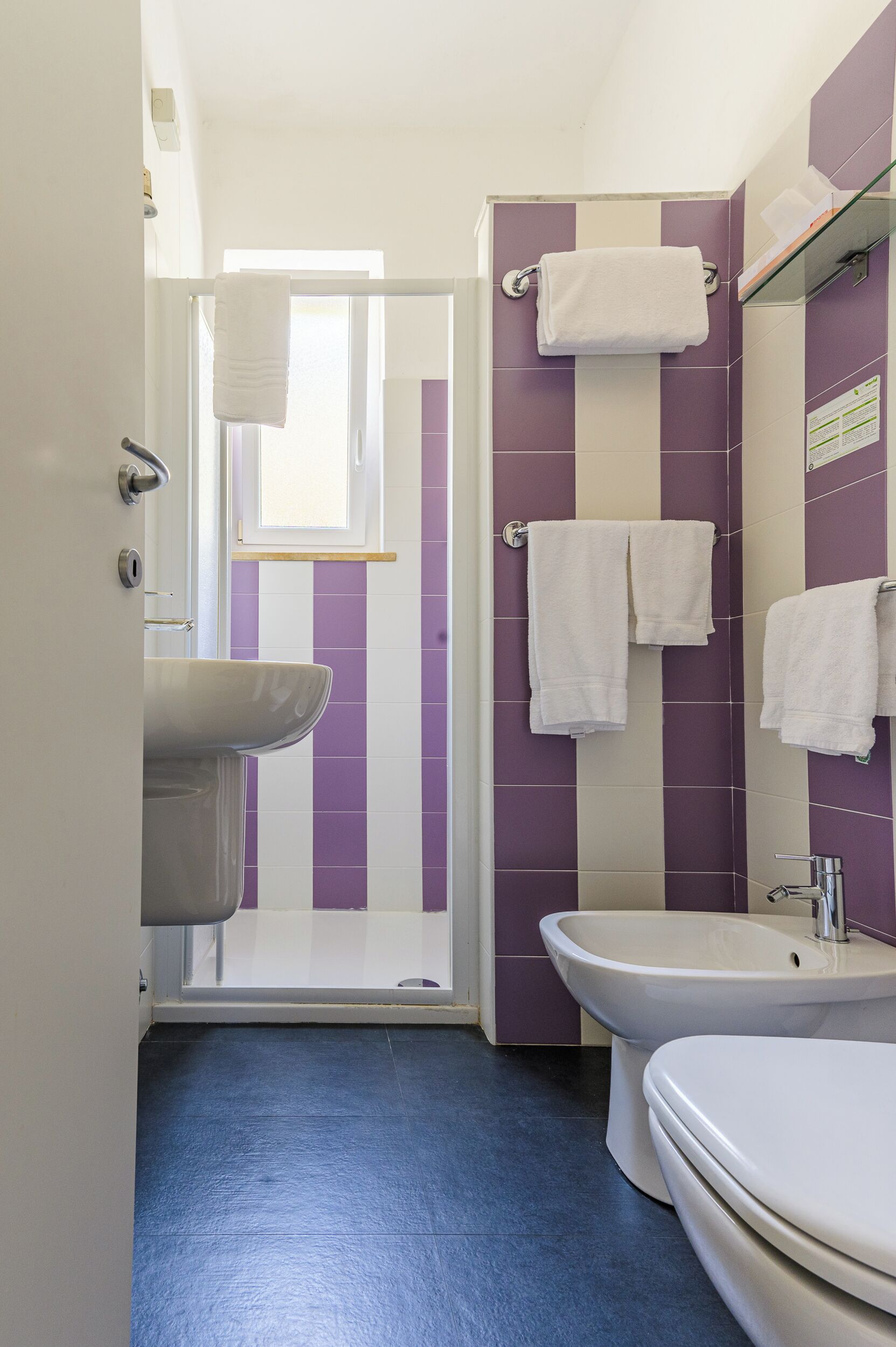 A bathroom with a shower, a sink, and a toilet. There are towels hanging on the wall.