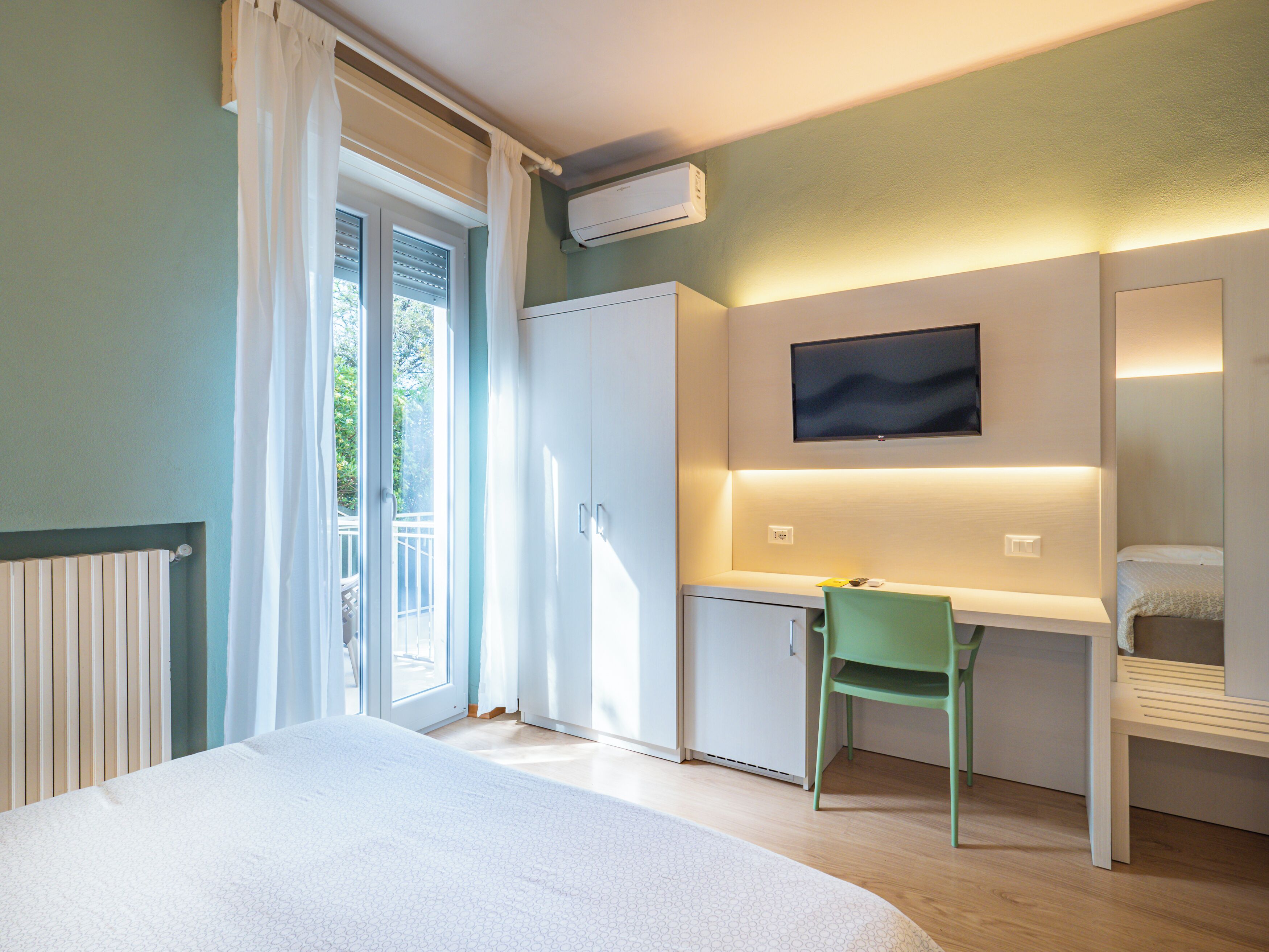 Un dormitorio con cama, escritorio, silla, televisor y ventana con cortinas.
