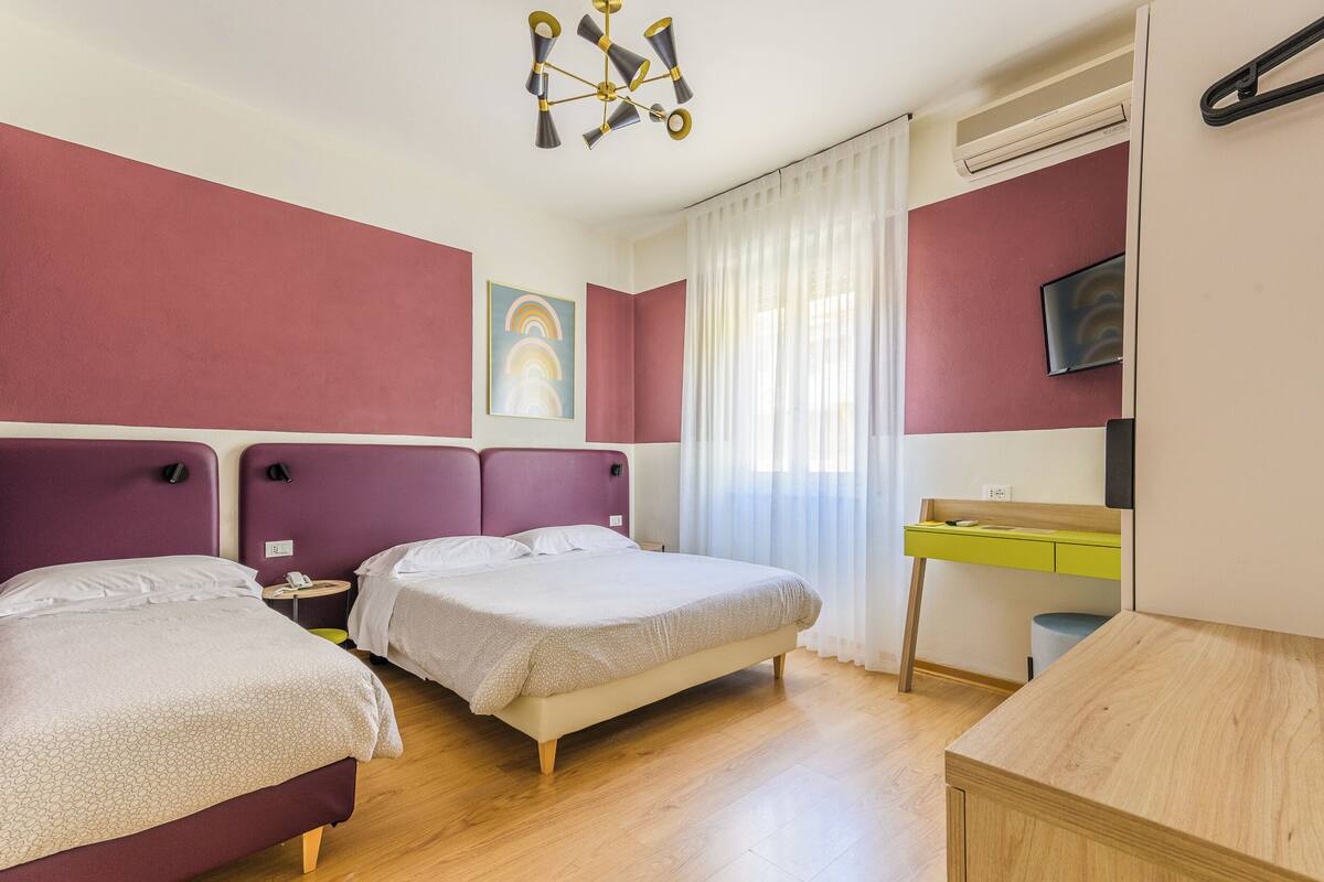 A hotel room with two beds, a desk, a chair, a TV, and a ceiling light.