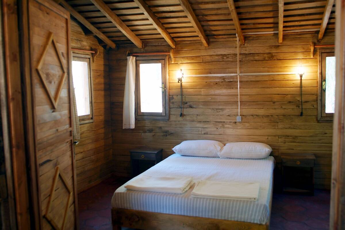 A wooden cabin bedroom with a bed, two bedside tables, and two wall-mounted lamps.
