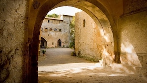 An arched stone corridor with a courtyard leading to a building with multiple windows and a door.