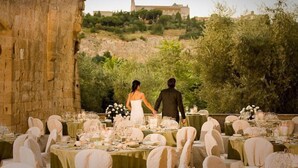 A wedding reception set in a historic stone building with tables arranged for guests, overlooking a lush landscape and a distant castle.