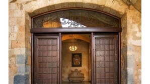 A stone archway with two wooden doors, a chandelier, and a bench.