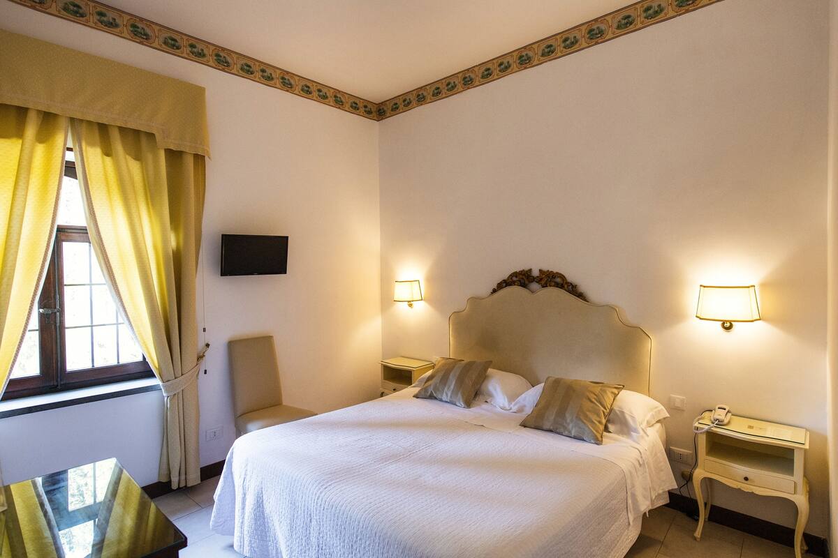 A neatly made bed with a headboard, two bedside tables with lamps, a chair, and a television on the wall.
