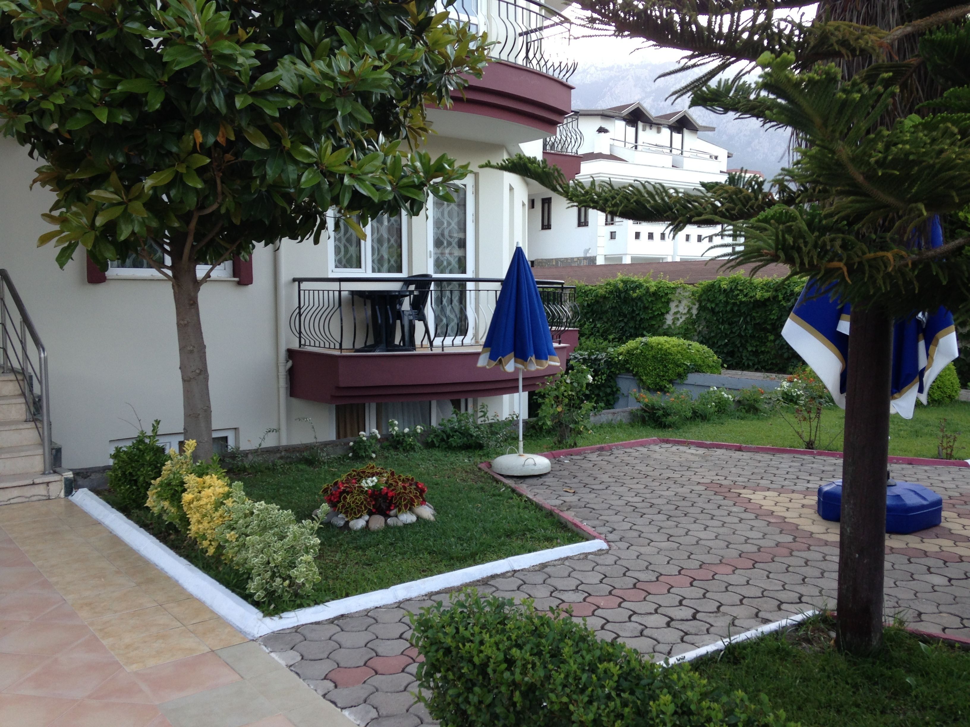 A residential building with a balcony, a garden with flowers, and a paved patio area.