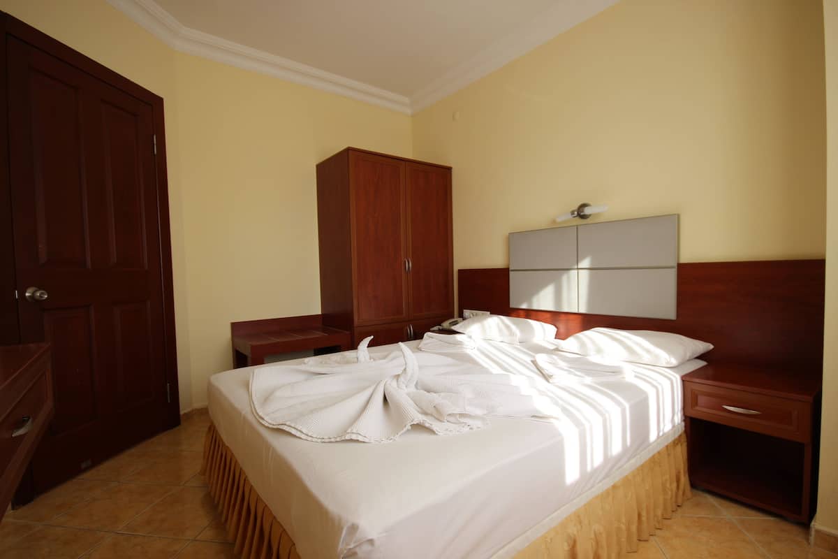 A hotel room with a bed, wooden wardrobe, bedside table, and a nightstand.