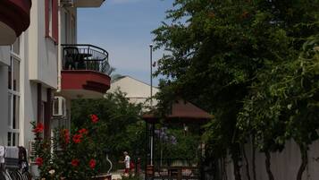 A courtyard with a building featuring a balcony, a pergola, and a garden with flowers.