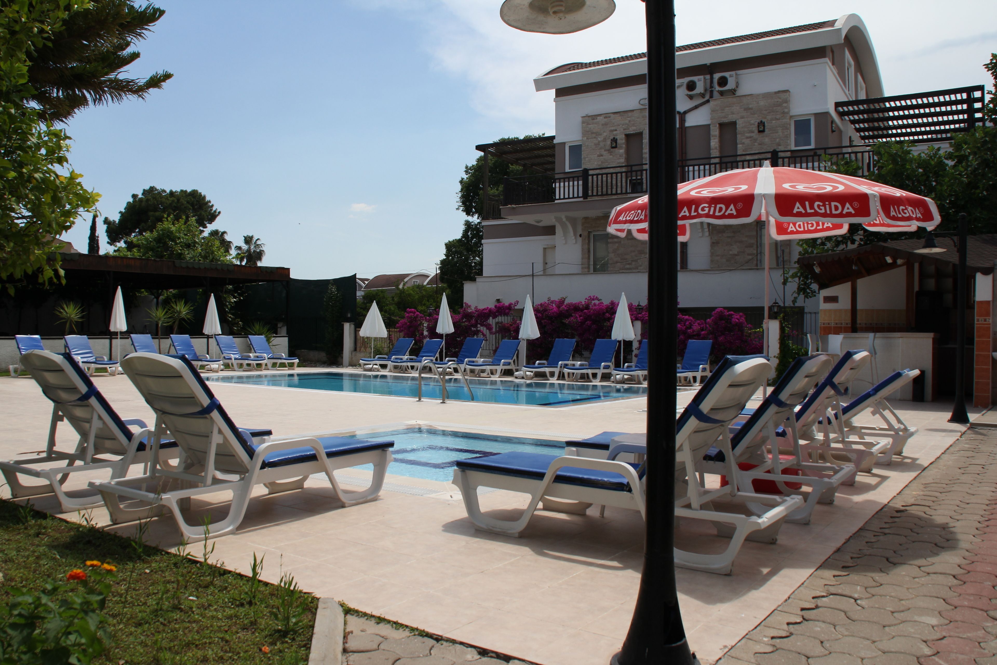 A poolside area with lounge chairs and umbrellas, a clear sky, and a building in the background.