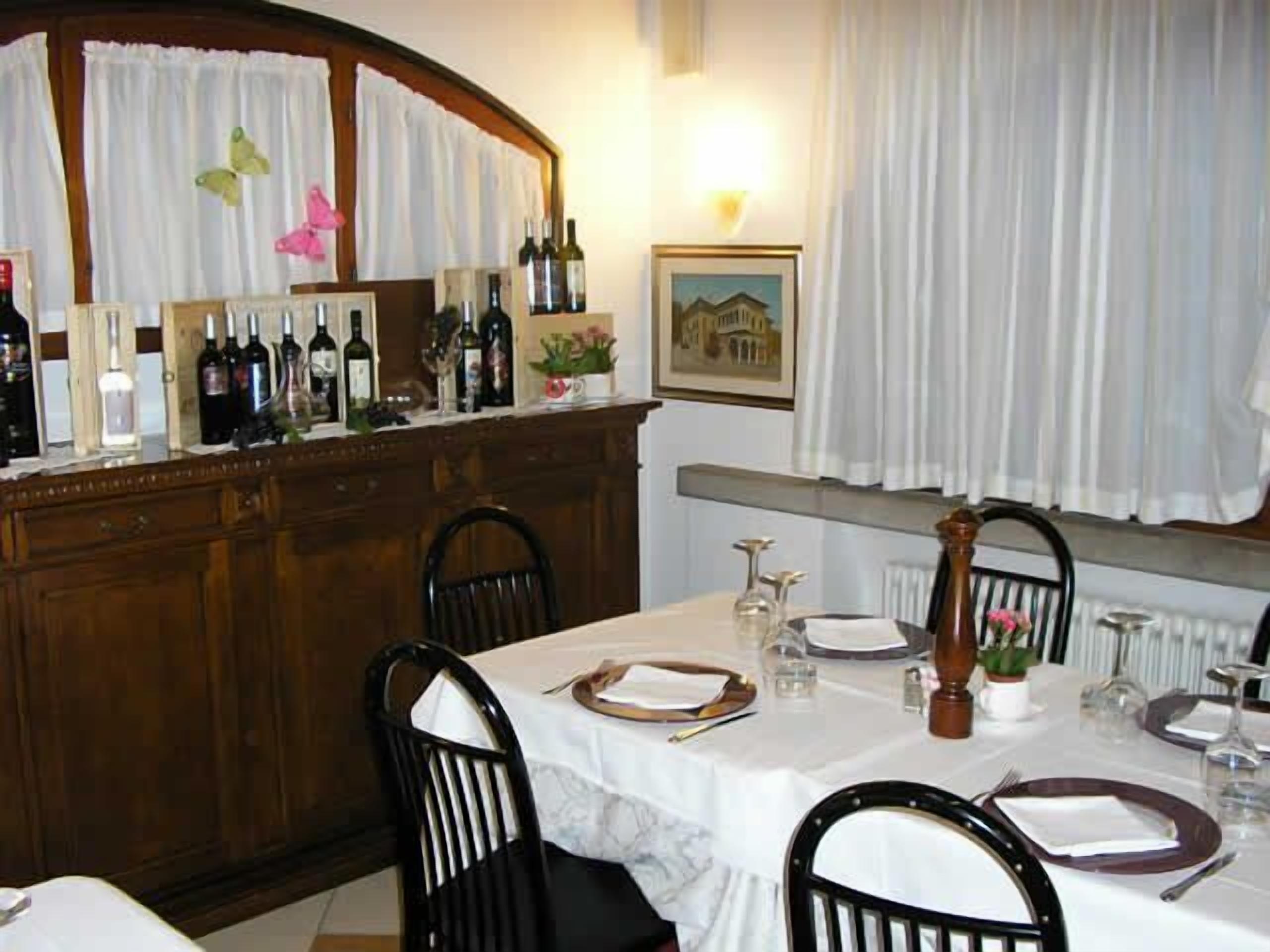 Un comedor con una mesa lista para cuatro personas, una barra con botellas de vino y una ventana con cortinas.