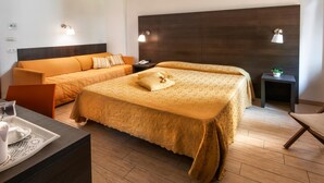 Ein Hotelzimmer mit zwei Betten, einem Sofa, einem kleinen Tisch mit Tablett und einem Nachttisch mit Lampe.