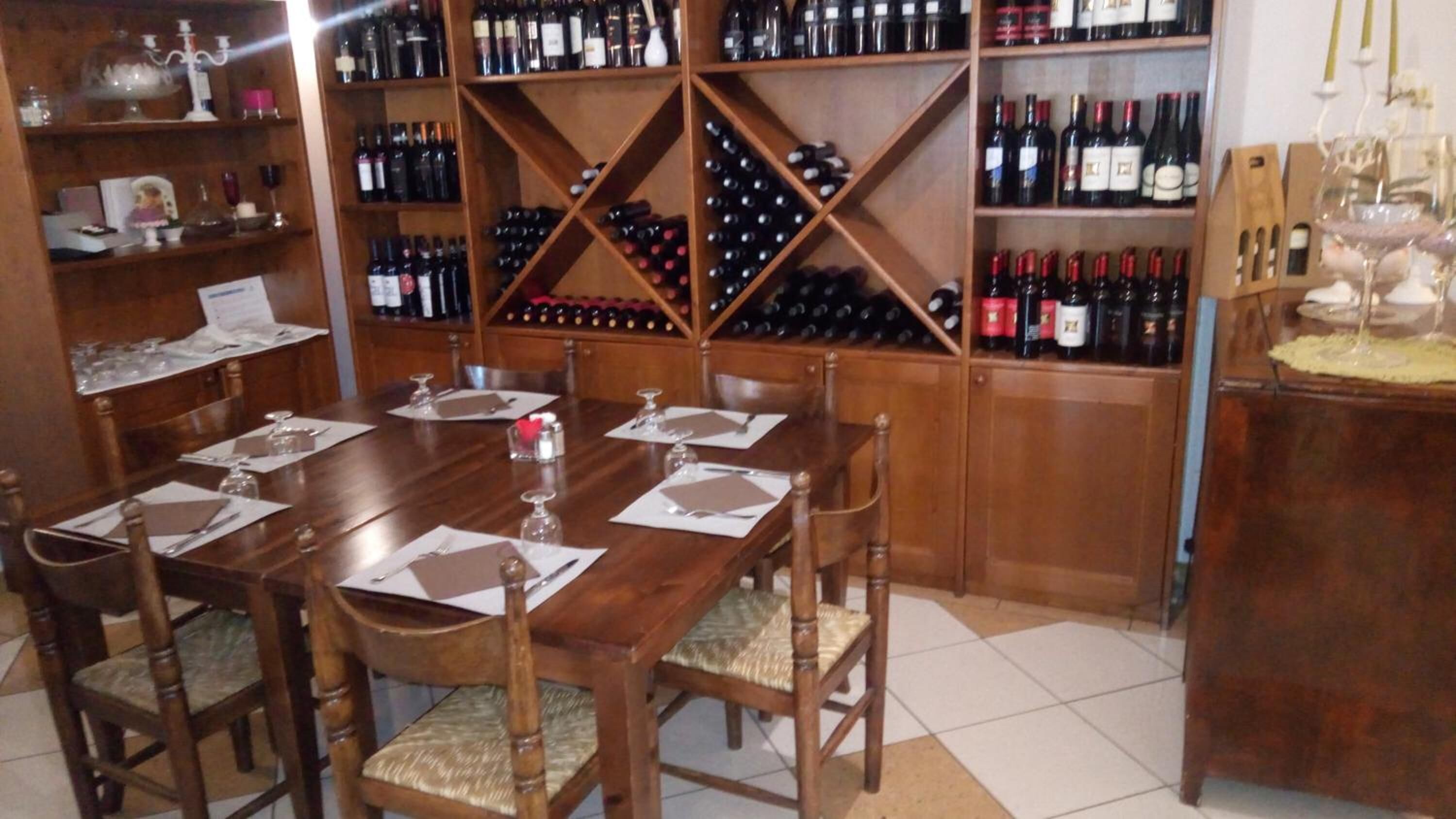 A dining area with a wooden table set for six, surrounded by chairs. A wine rack with multiple bottles is in the background.
