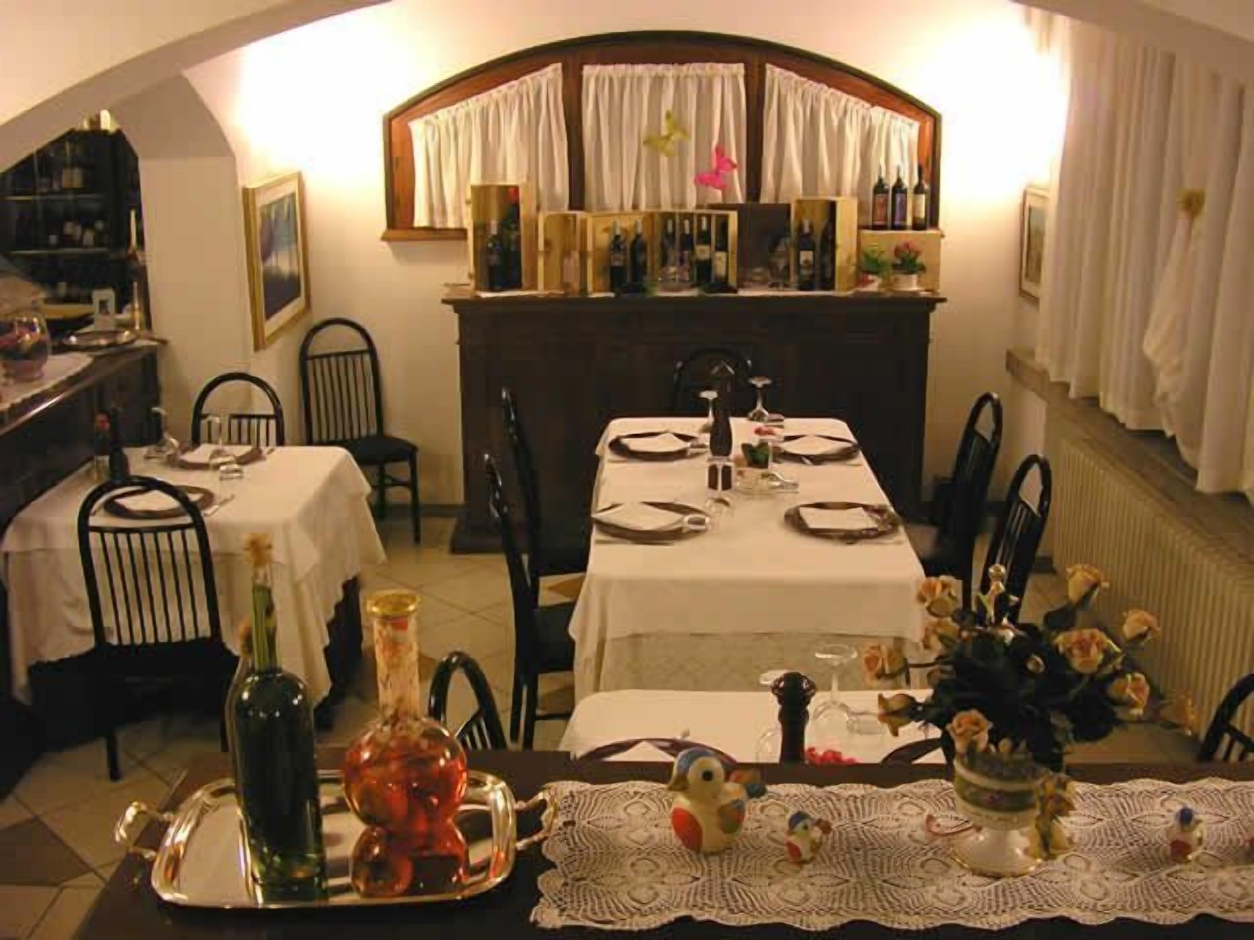 A dining area with two tables set for four, each with white tablecloths, black chairs, and a central vase with flowers.