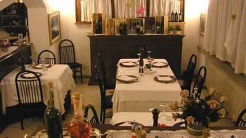 A dining area with two tables set for four, each with white tablecloths, black chairs, and a central vase with flowers.